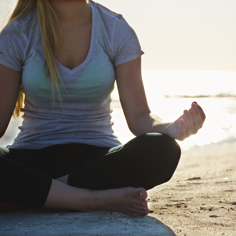 Woman meditating on the beach while waves crash.