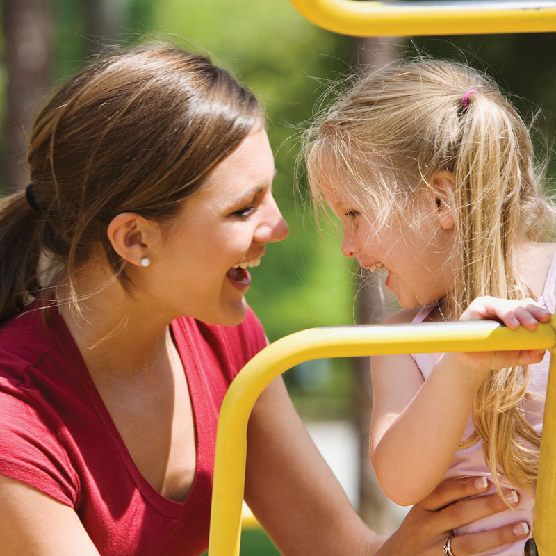 Mother and child playing at playground laughing together.